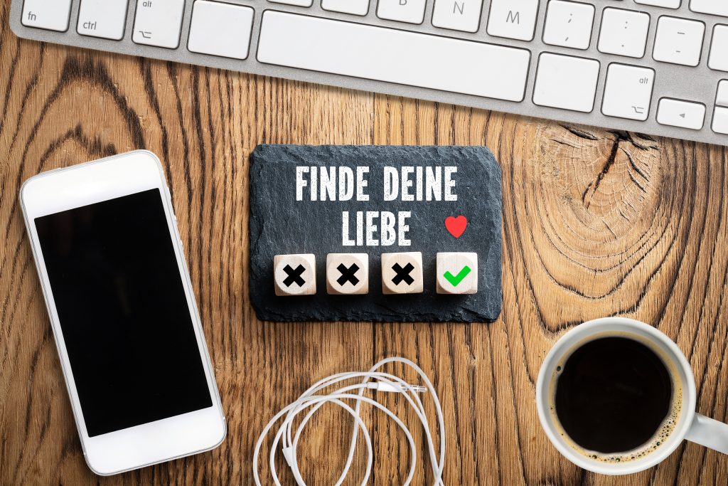 Tastatur und Smartphone auf einem Holztisch, dazwischen eine Schieferplatte mit der Nachricht "Finde Deine Liebe"