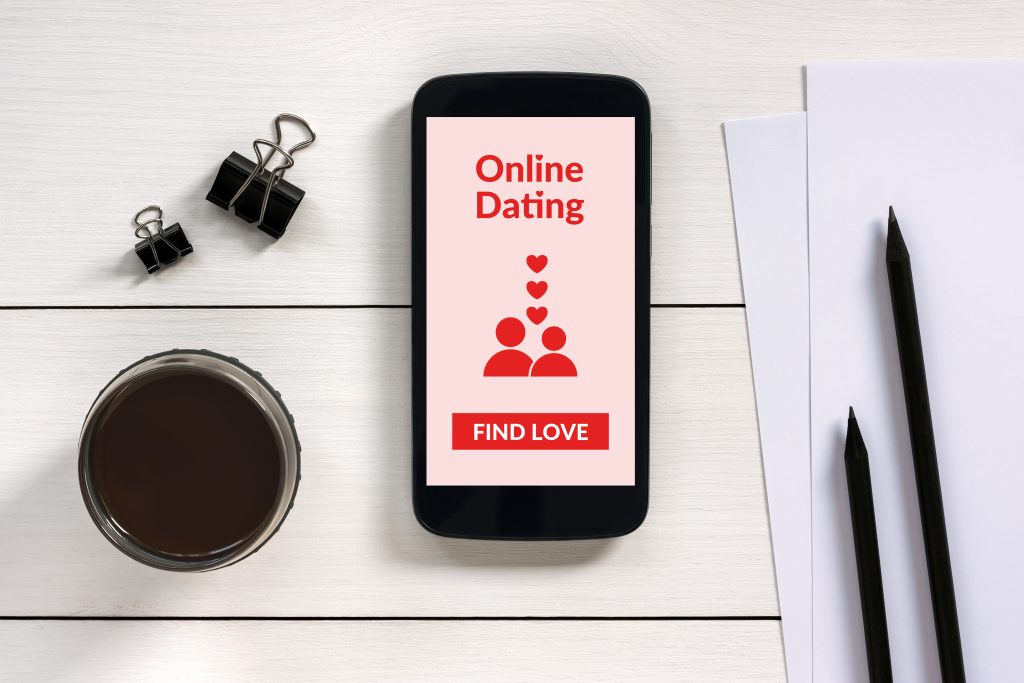 Online-Dating App auf einem Smartphone, welches auf einem Tisch mit weiteren Utensilien liegt